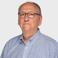 A middle-aged man with short hair and glasses, wearing a blue and white checkered button-up shirt, poses against a plain light background. EFESO Management Consultants